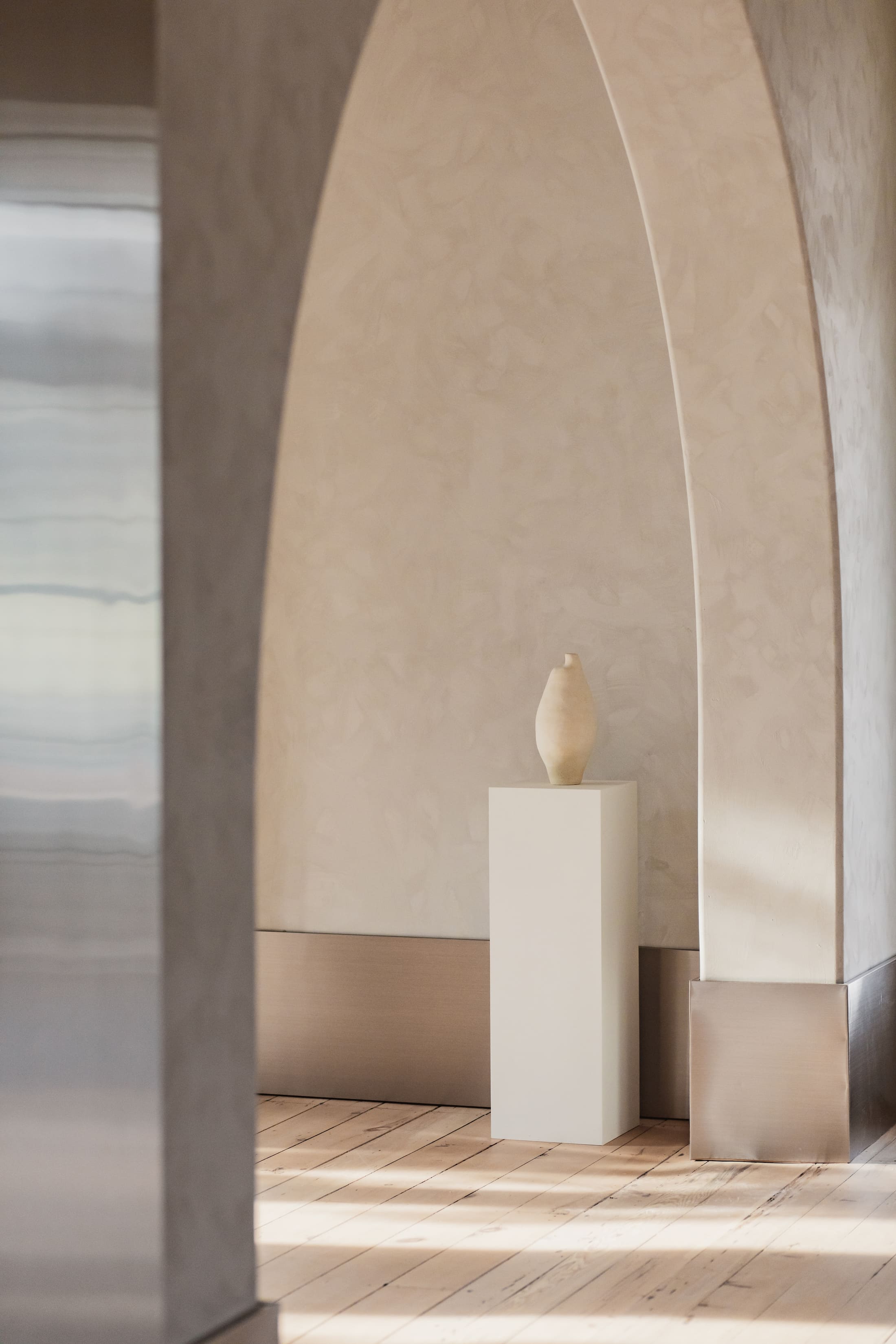 a pillar with a vase on it, sitting in a bright room with warm wood floors