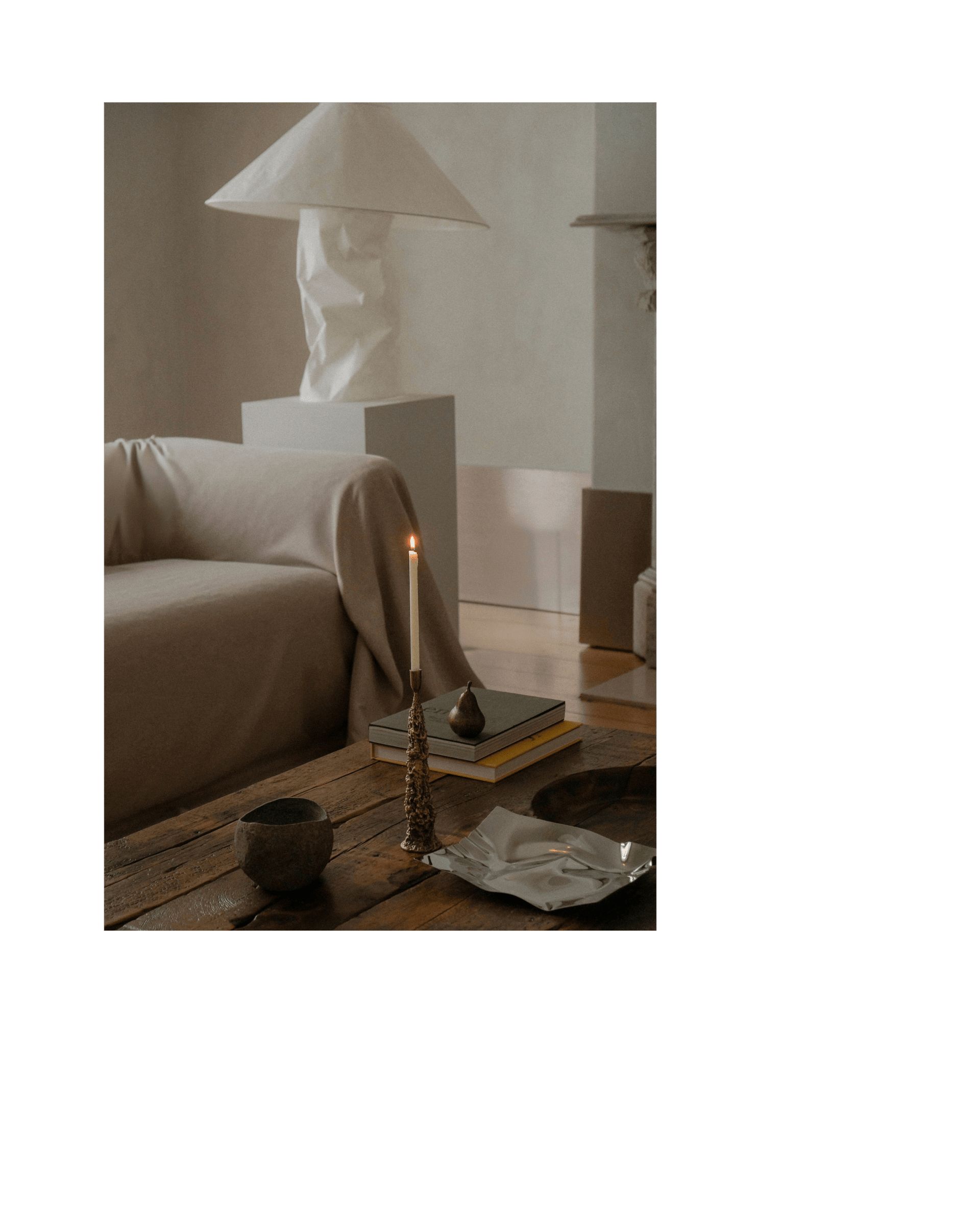 A lit candle in a gold decorative candle holder sits on a coffee table amidst various objects