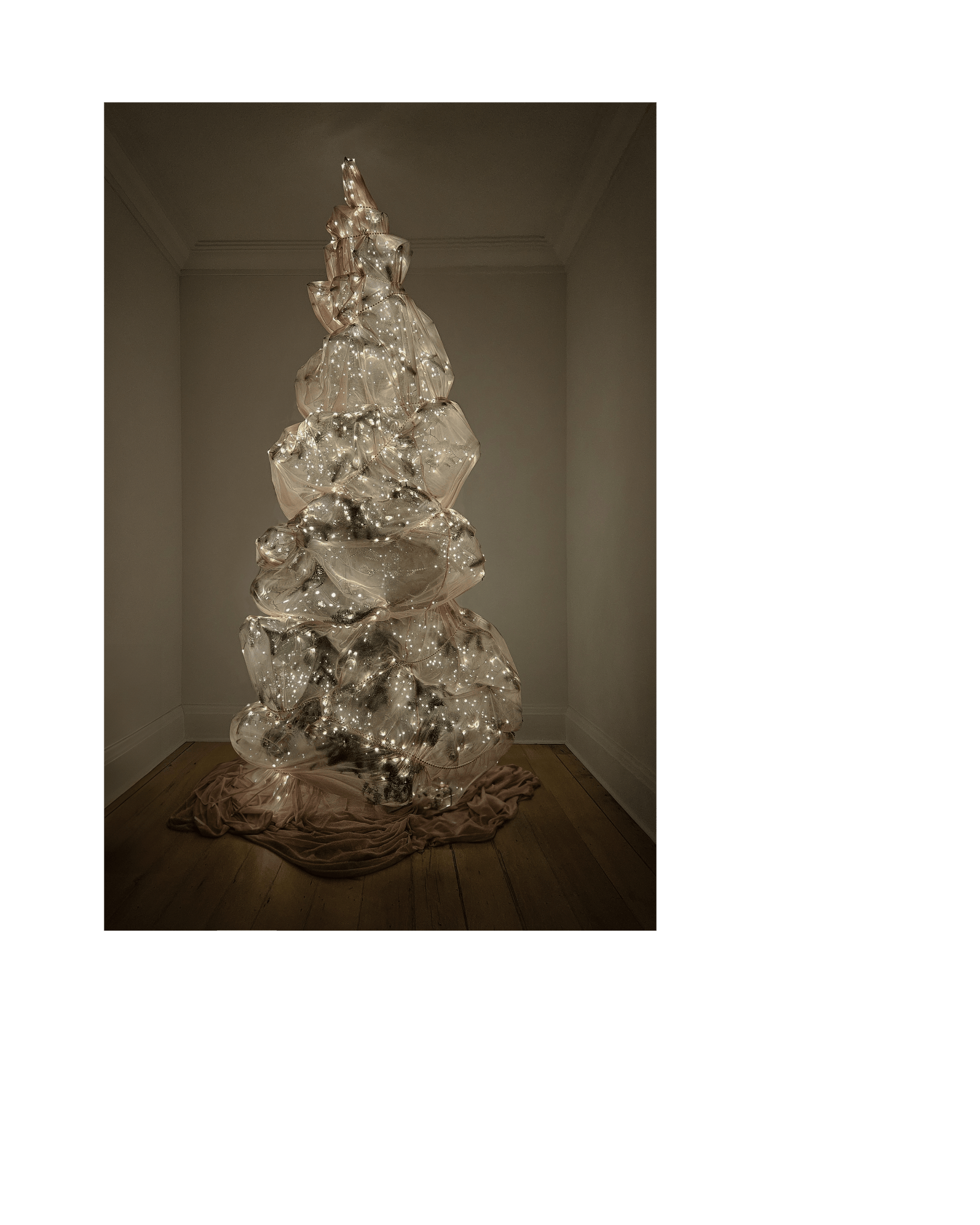 A christmas tree is wrapped in sheer pink fabric, lights glowing underneath