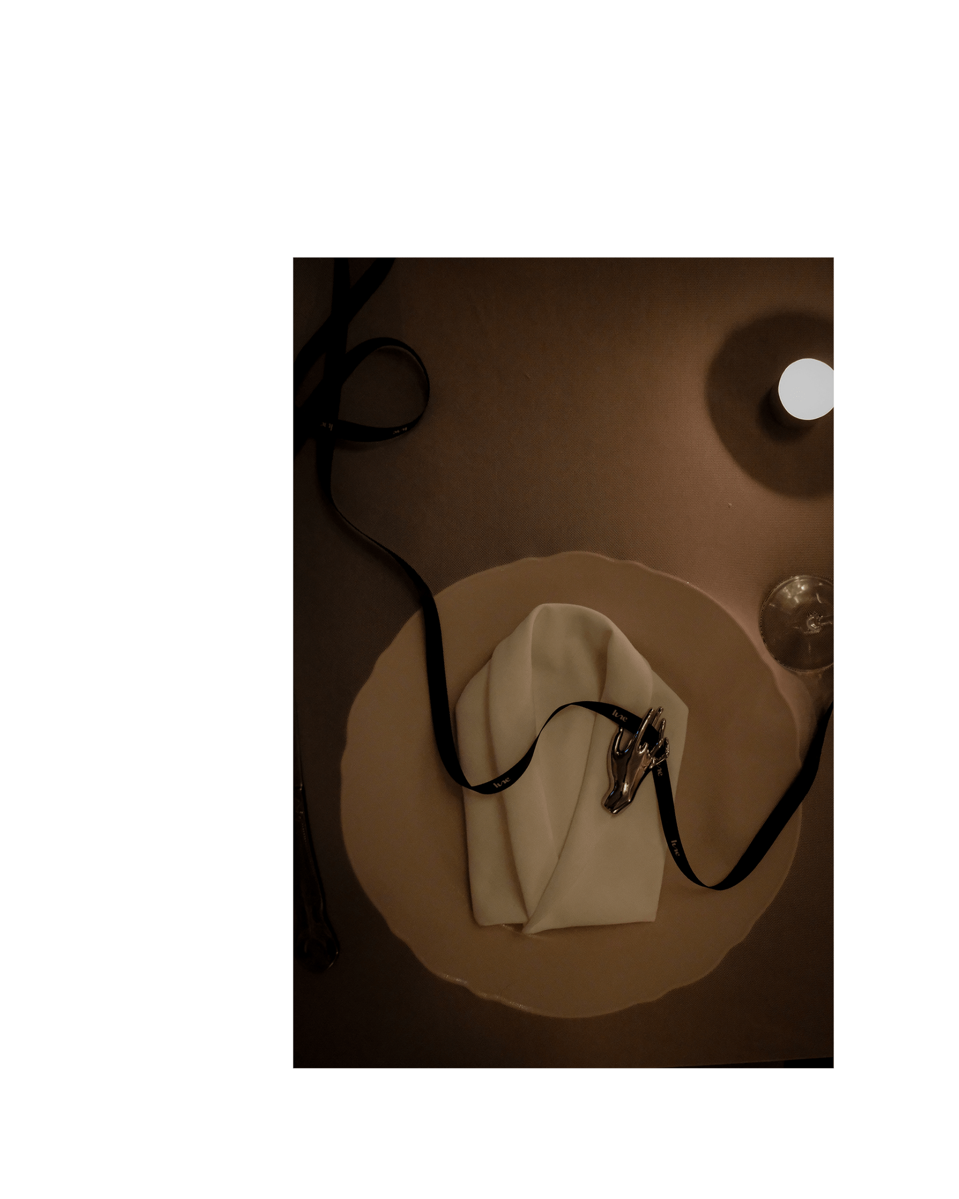 A napkin folded into a shirt sits on top of a plate, a black Lune branded ribbon curls across the plate