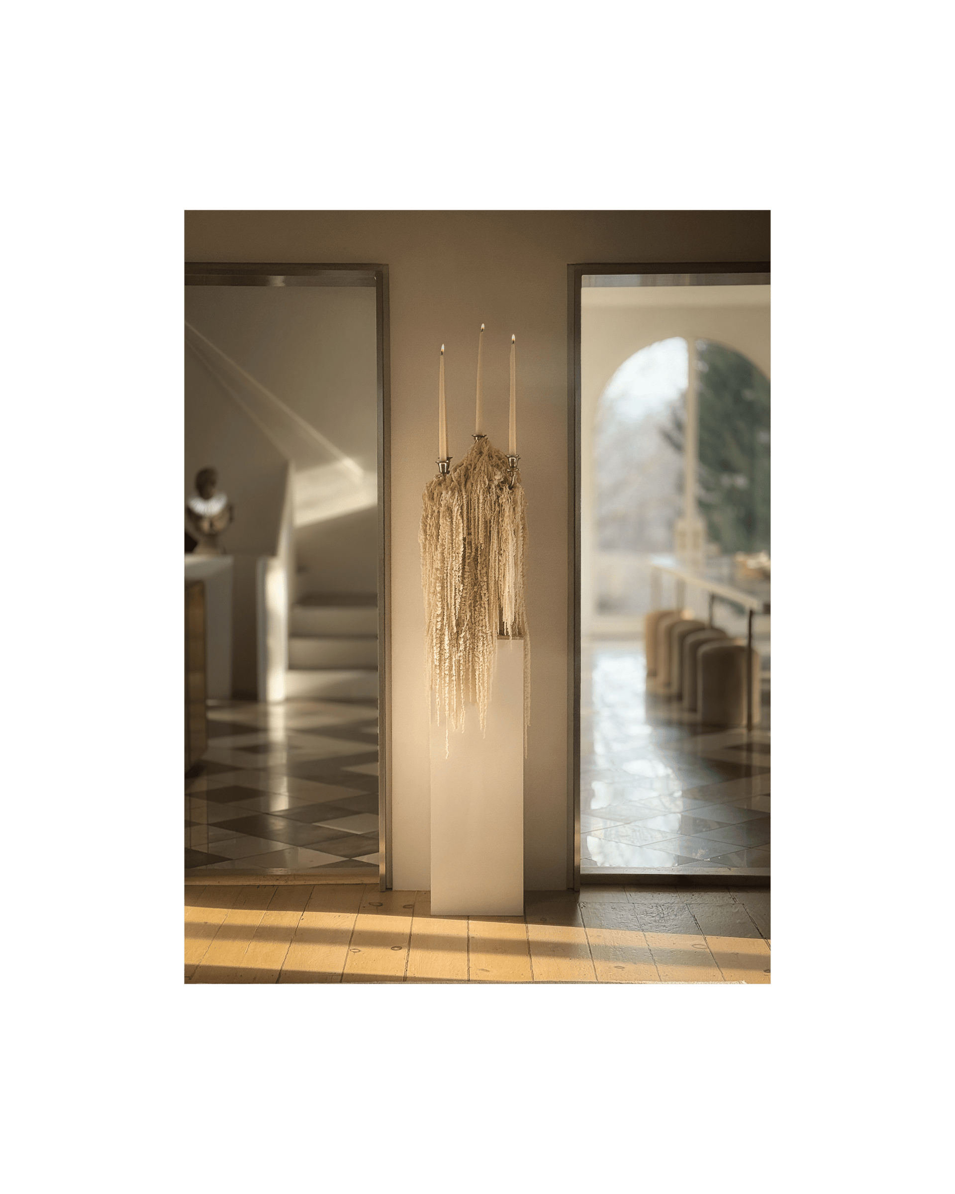 A lit candelabra dripping with Hanging Amaranthus flowers sits on pedestal between two doorways
