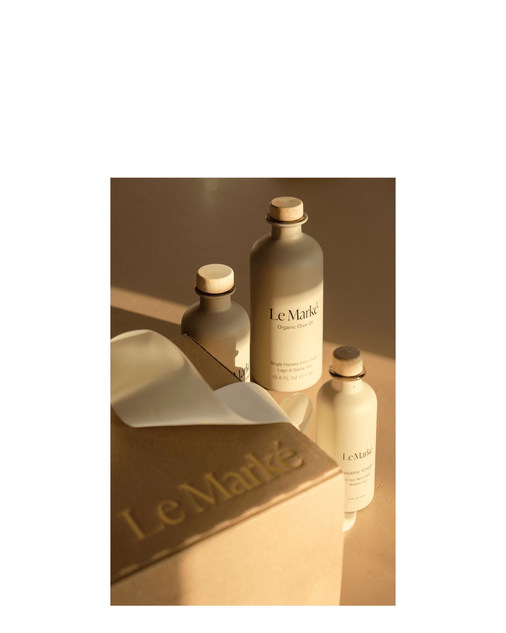 Three Le Marke bottles sit in the sunlight, a branded box and ribbon can be seen in the foreground