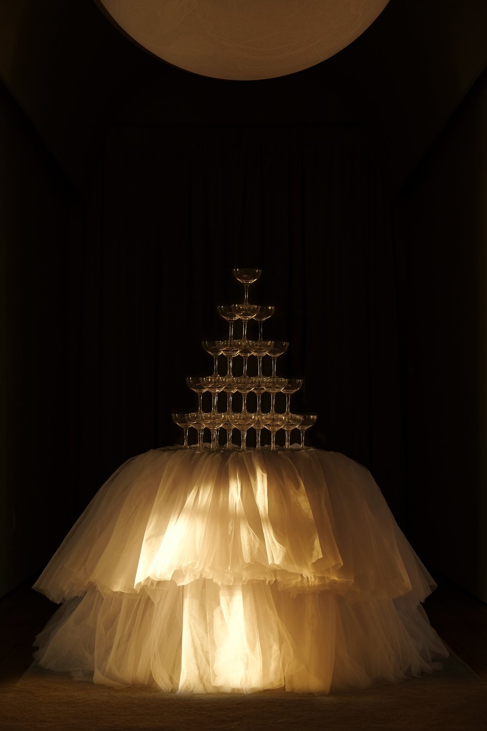 A champagne tower sits on top of a table with a voluminous tulle tablecloth