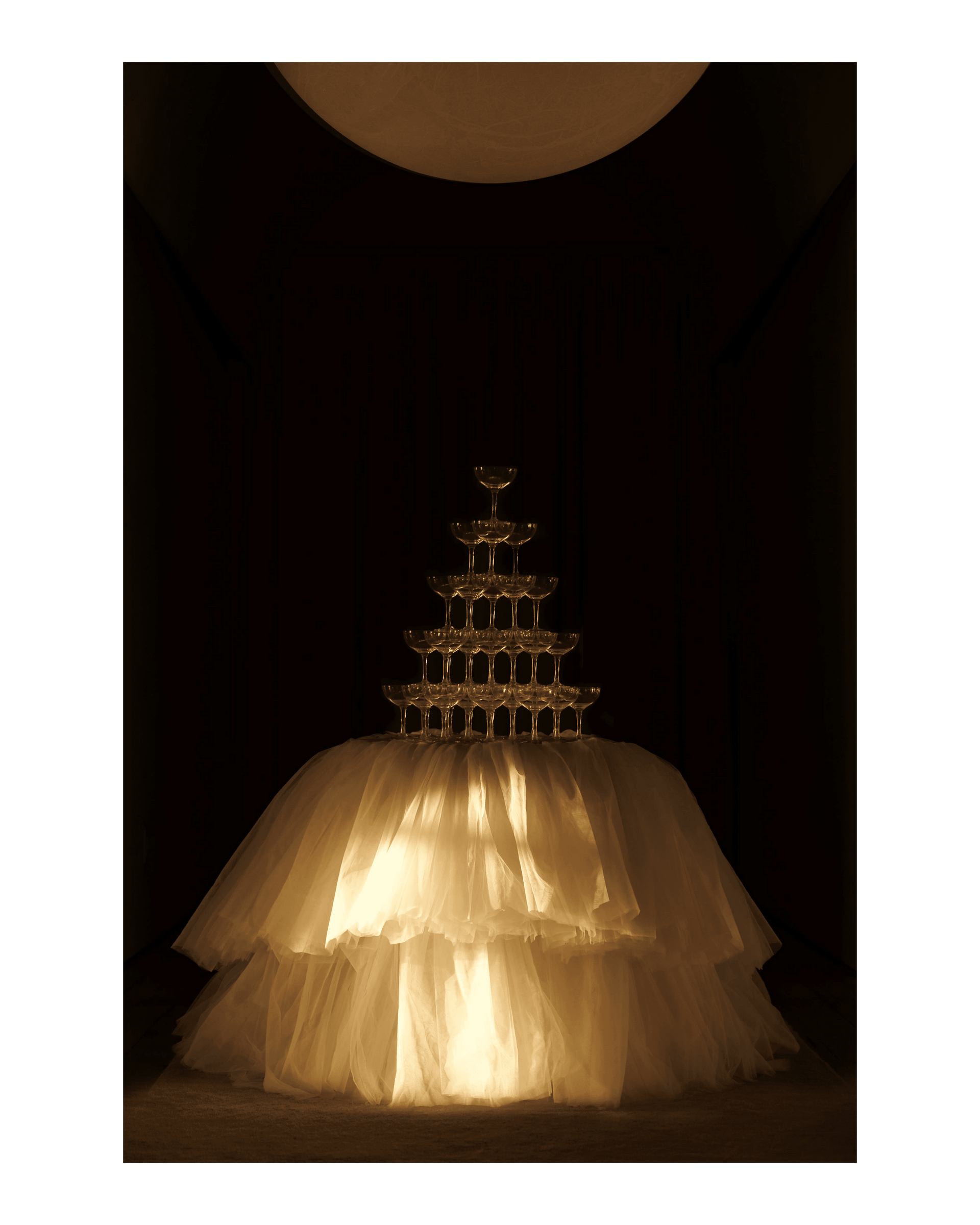 A champagne tower of coupe glasses sits on top of a table covered in a bespoke tablecloth.