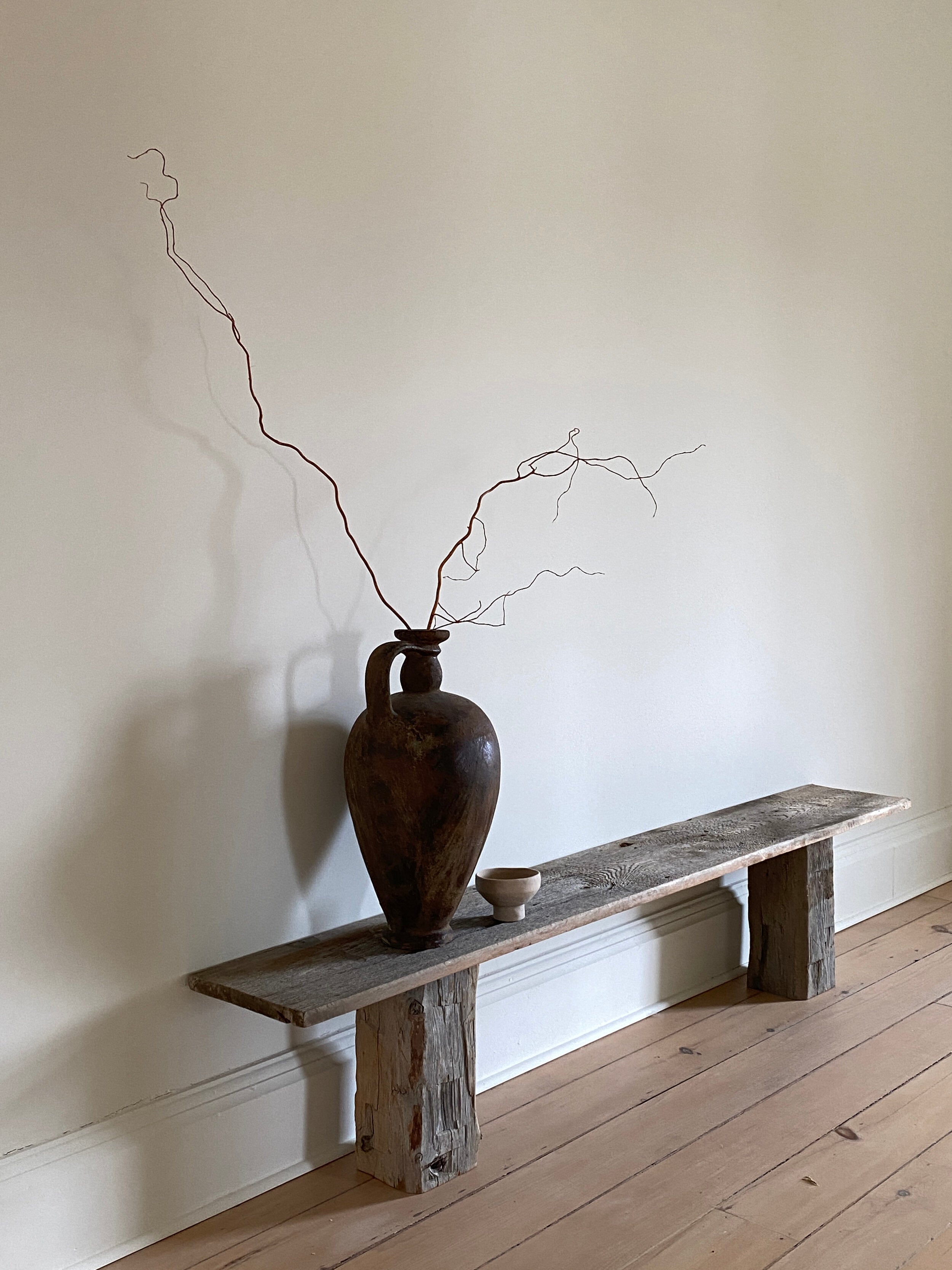 long wood bench with large black vase on it