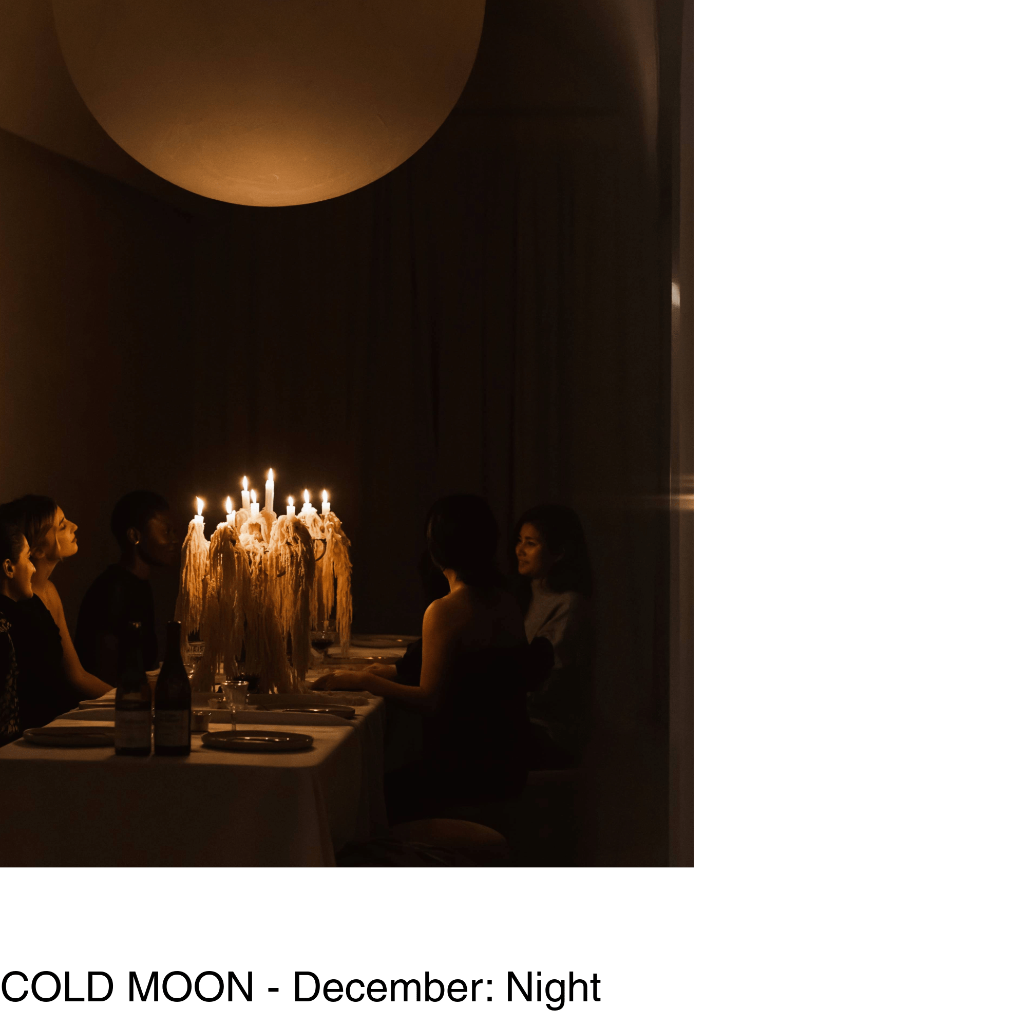 guests sit at a table in the glow of a lit candelabra under a large moon shaped pendant