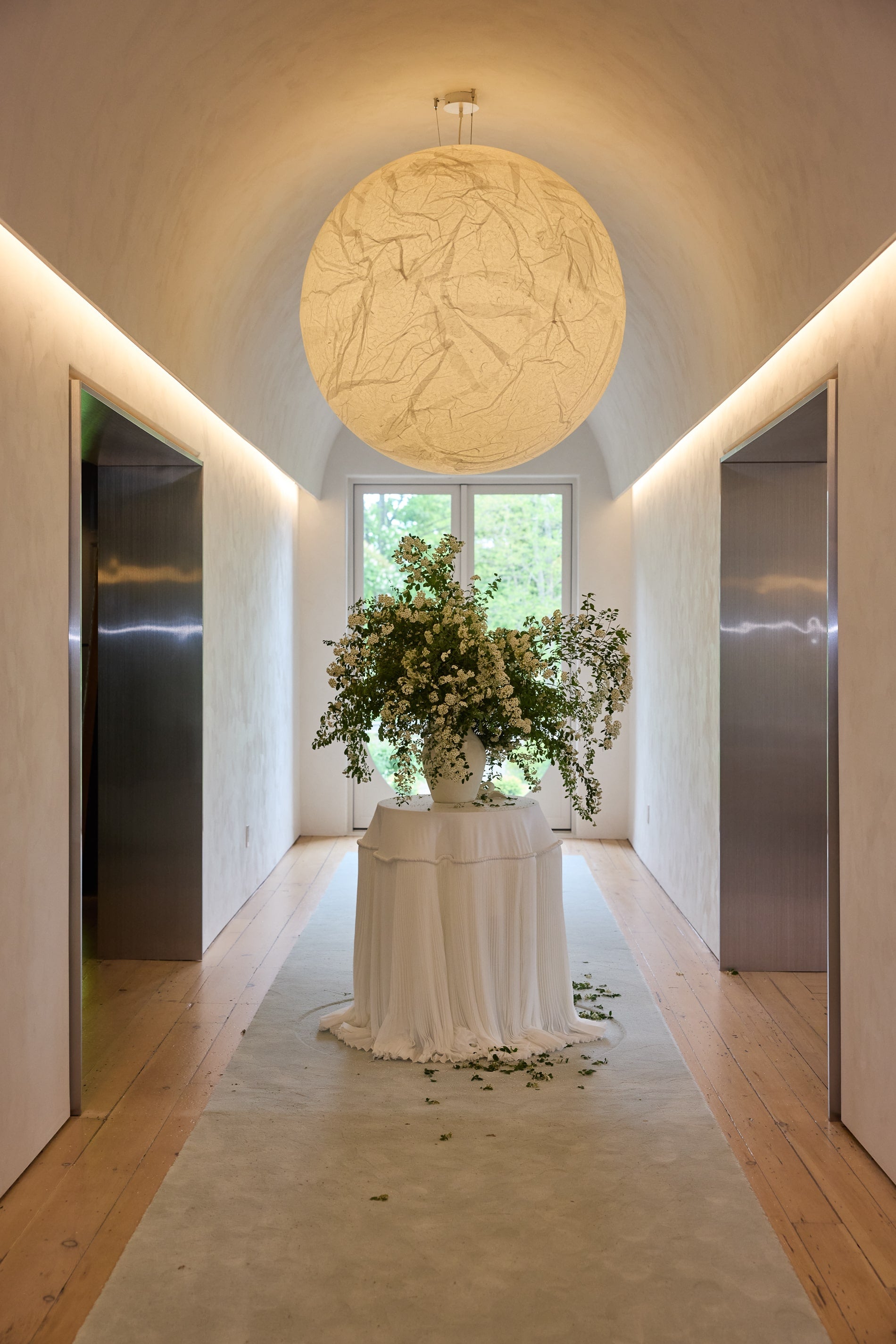 Large vase of flowers sits under large moon shaped pendant in bright hallway