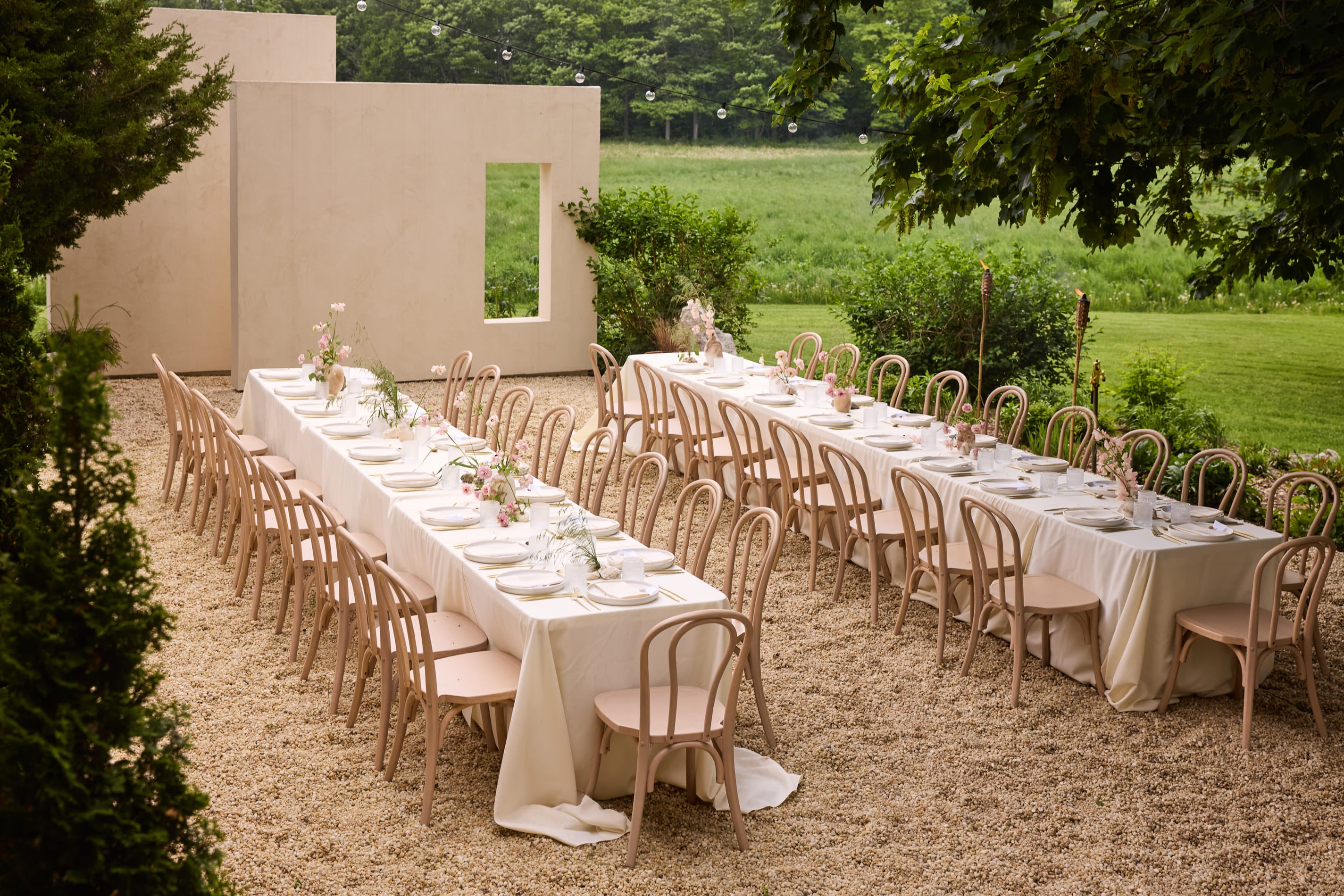 Two long tables are set on a european style terrace. Summer gardens surround the area.