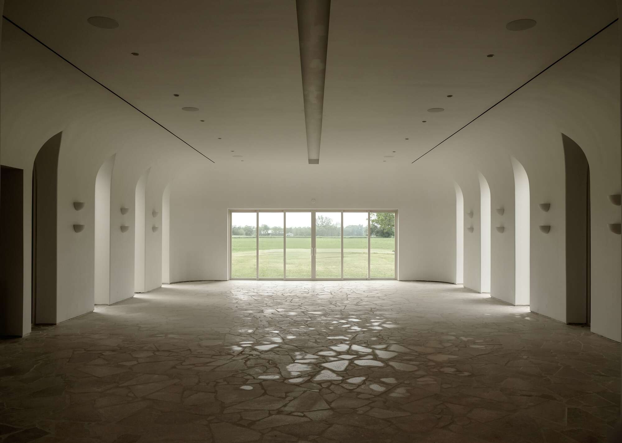 wide open venue with large glass doors at the far end, tall windows on either side and a flagstone floor