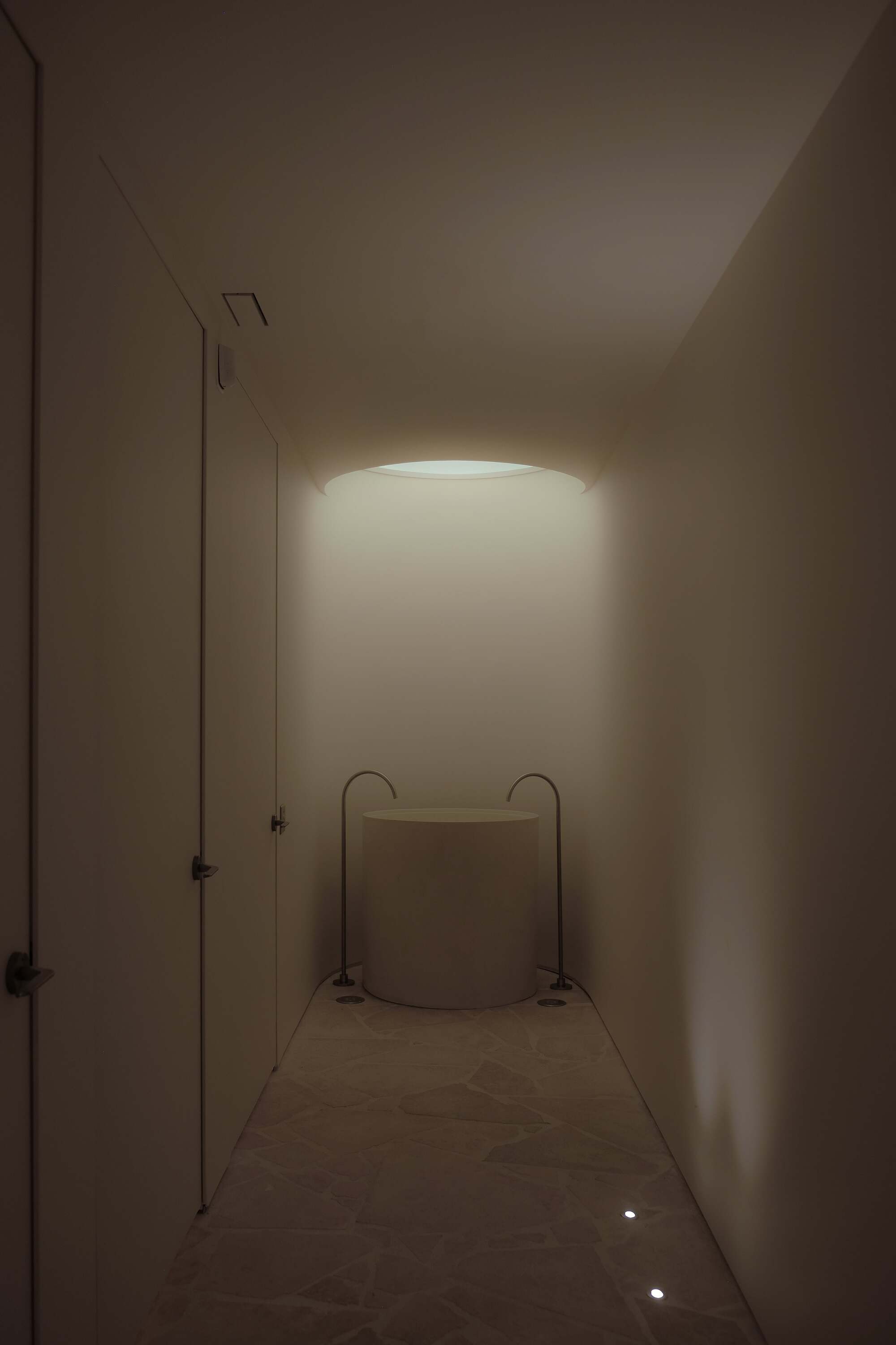 circular sink sits under a skylight at the end of a hallway in subdued light