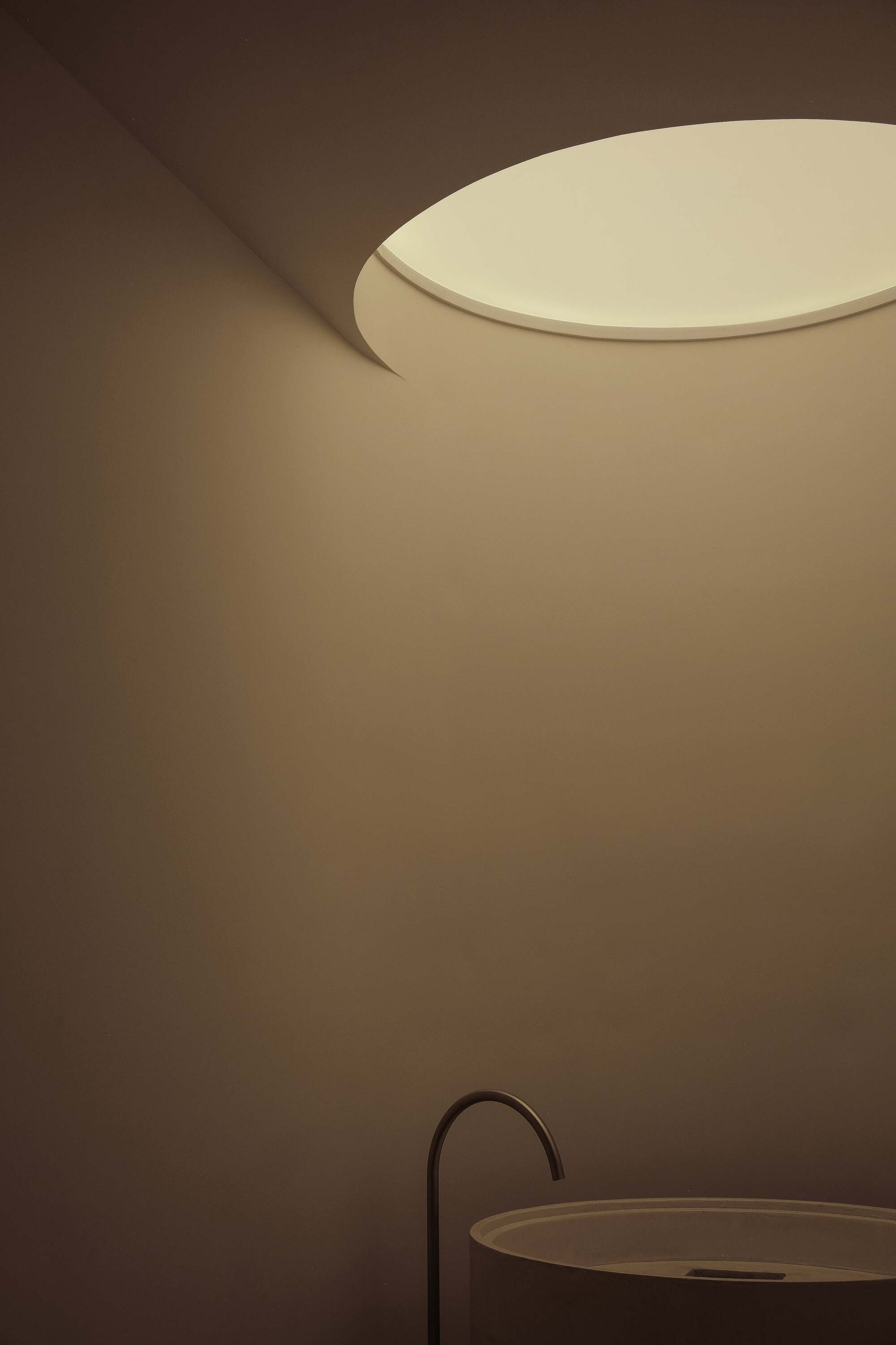 round skylight sits above circular sink with minimalist water faucet