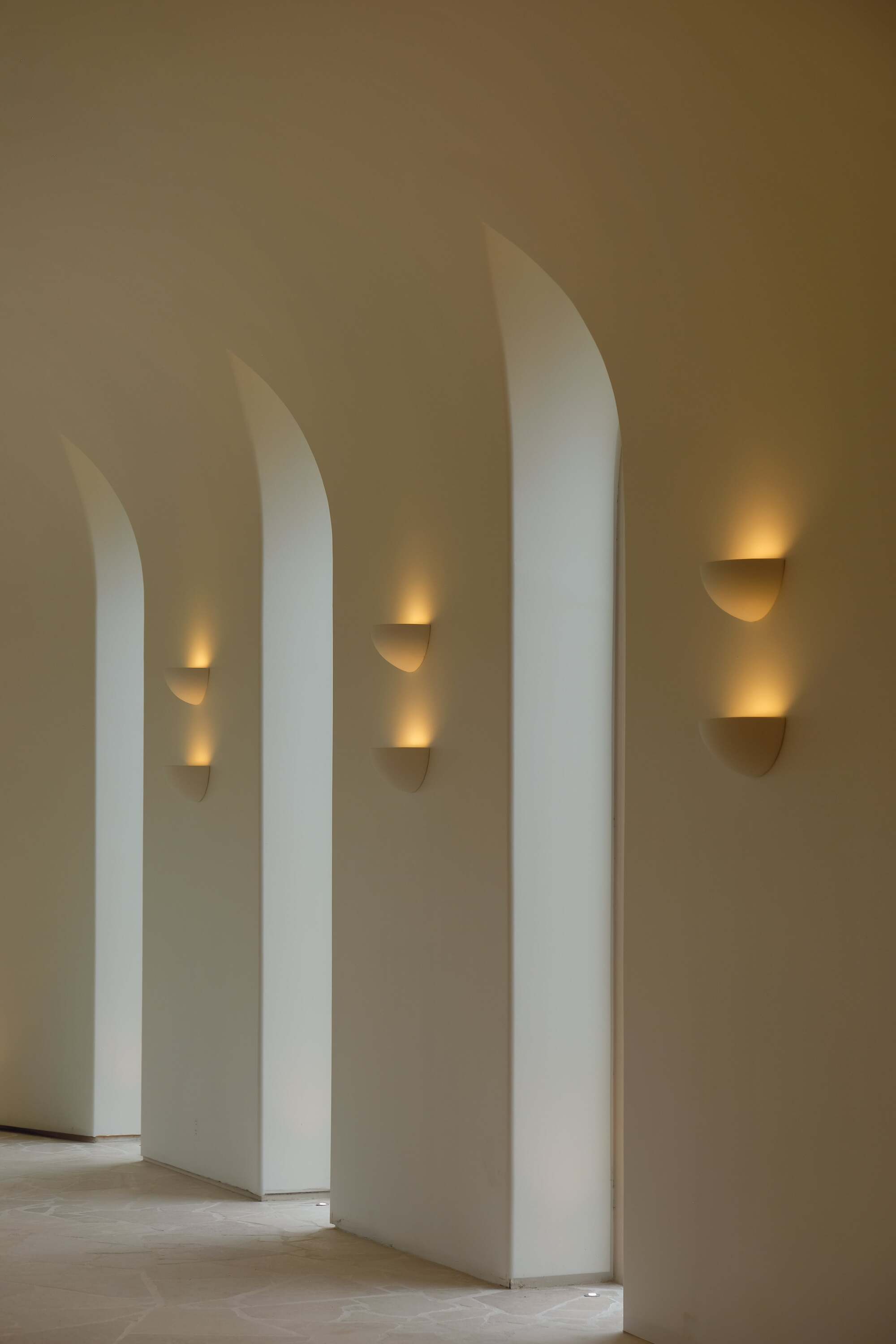 tall cathedral style windows with light streaming in, glowing sconces sit on the wall in between them