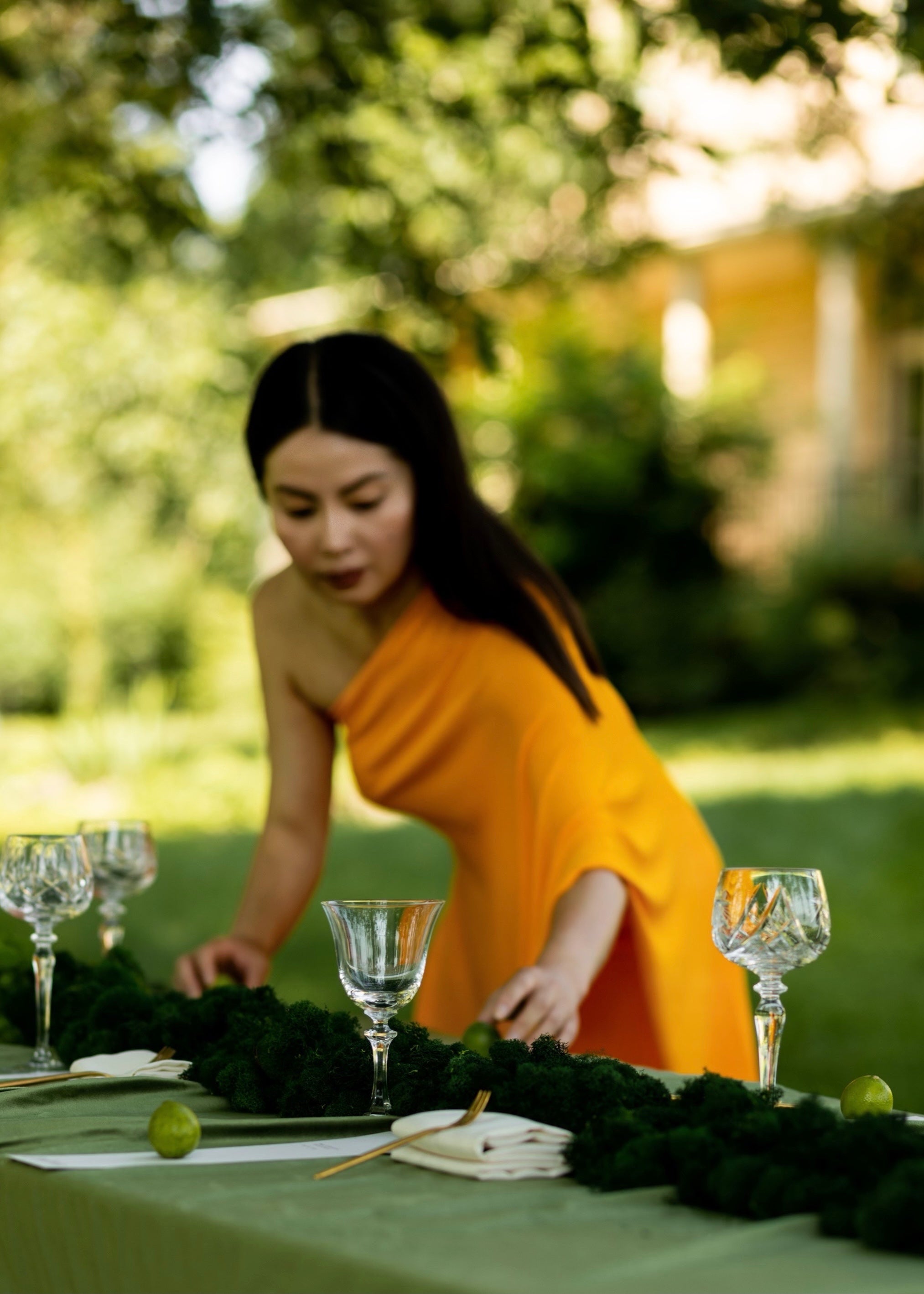 woman in orange dress places finishing touches on a long table set with a green velvet tablecloth