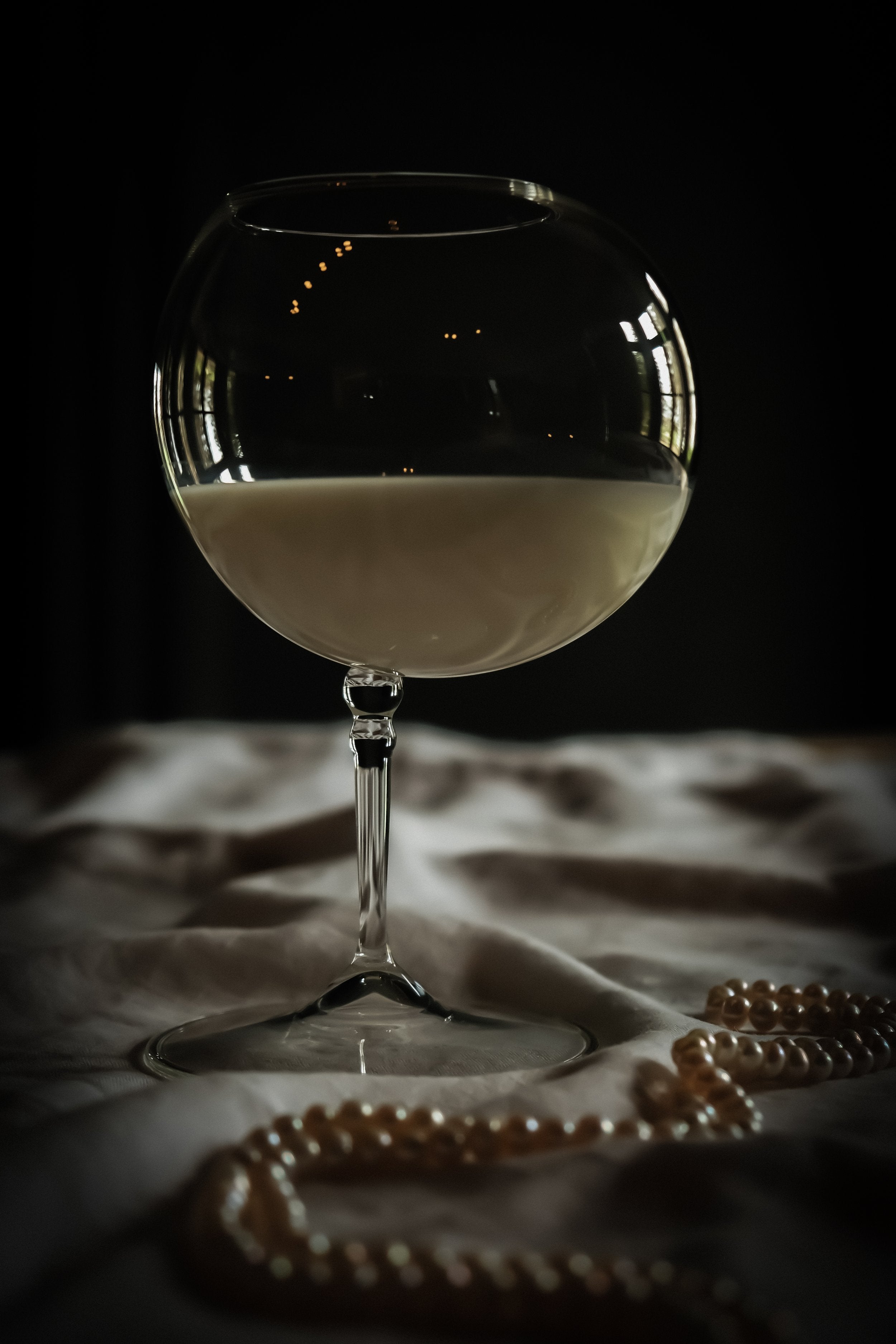 bubble shaped wine glass, a string of pearls sits in front