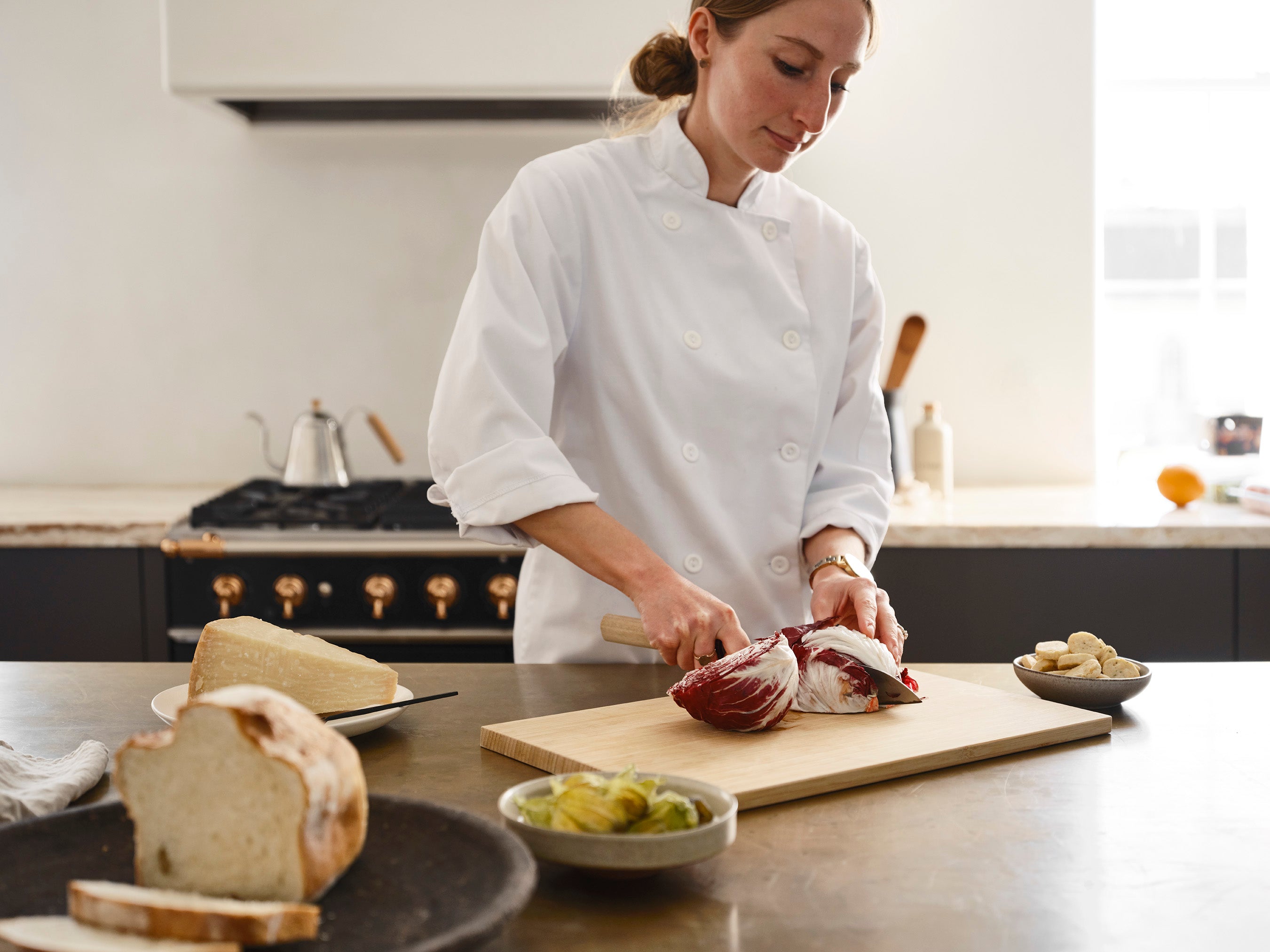 Chef Jaclyn Shewchuk slices raddichio on a cutting board in the kitchen at Lune 1860, a few small bowls of other ingredients are placed n the countertop beside her.