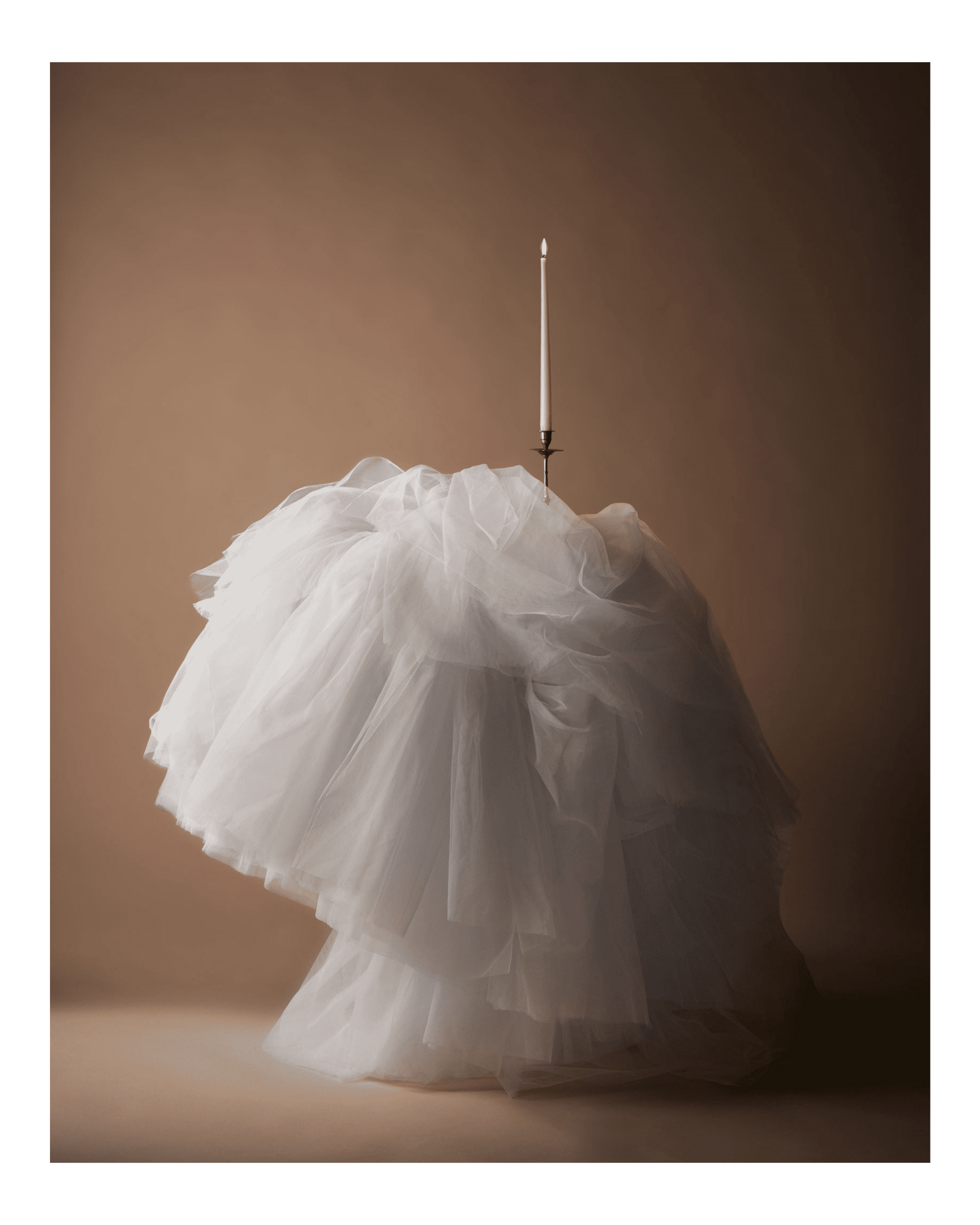 A tall candle in a silver candle holder sits on top of a bespoke tablecloth.