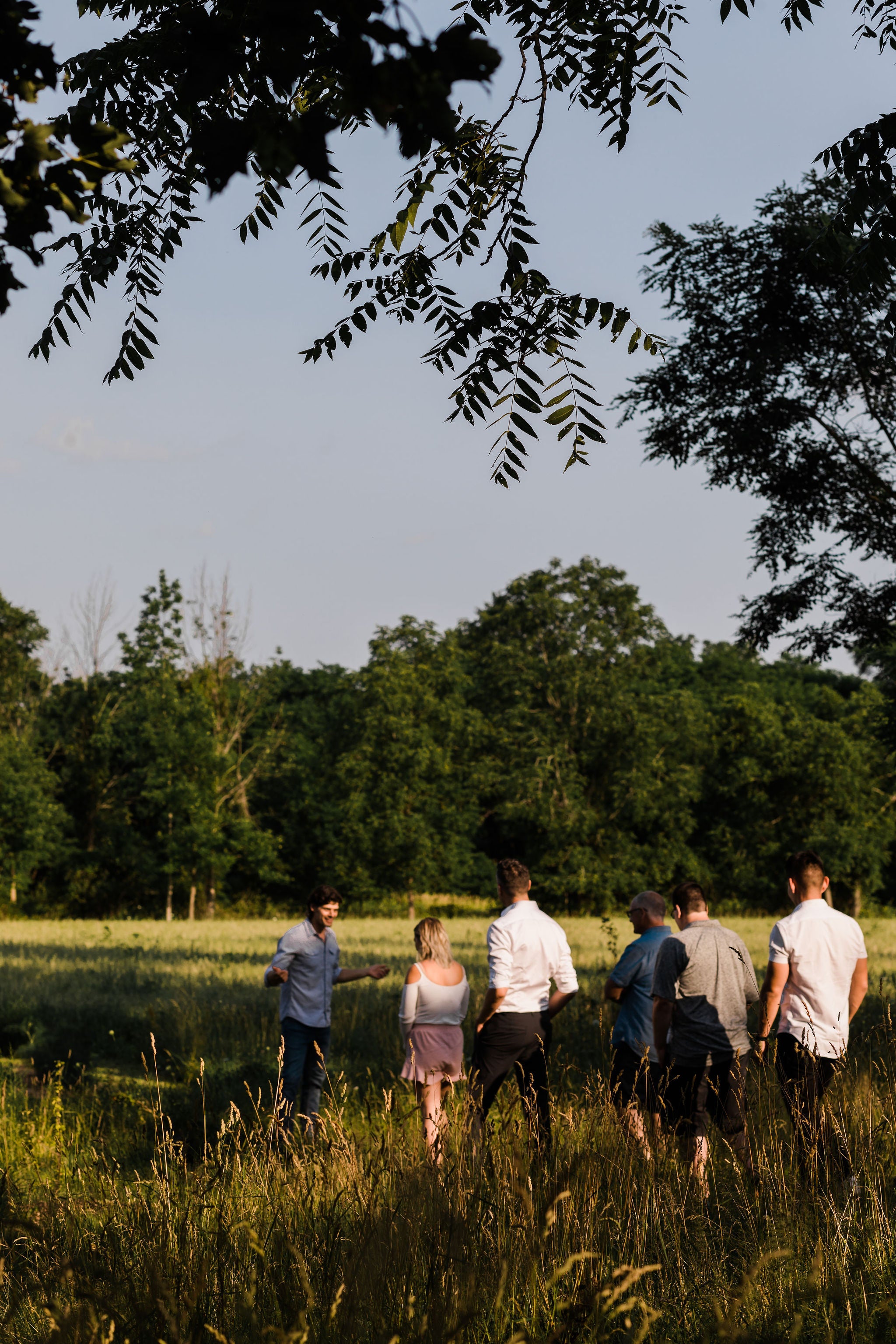 man stands outside in front of a field, giving a garden tour to a group of guests