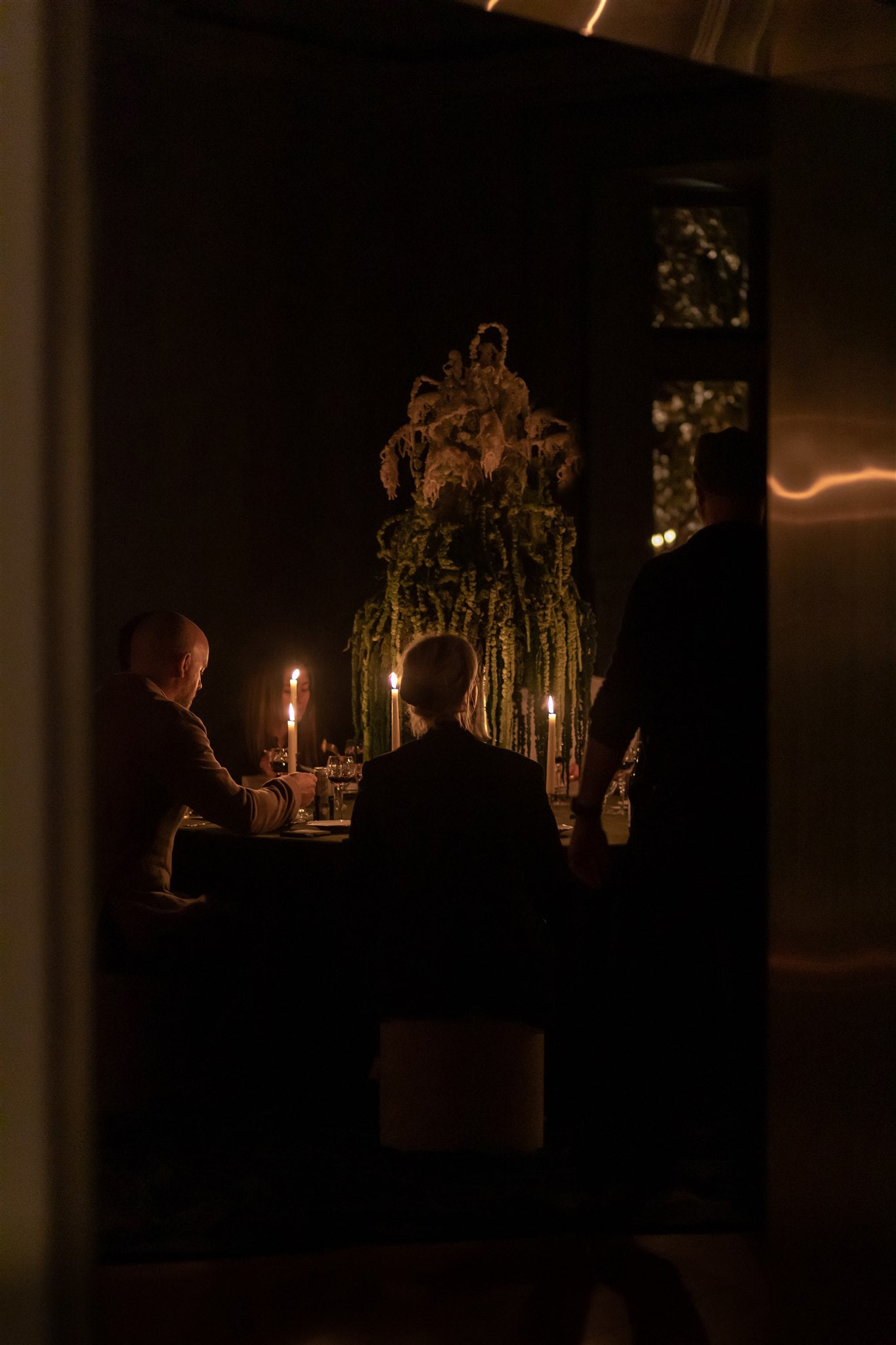 guests huddle around a candlelit table, a large amaranth arrangement in the middle
