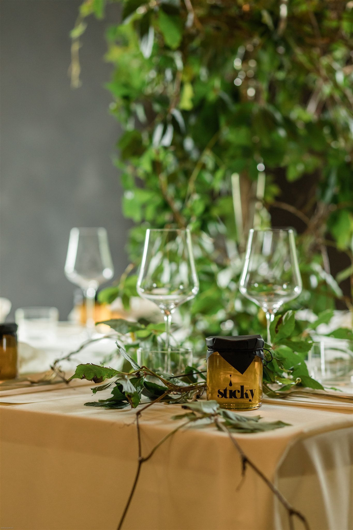 jar of Sticky honey sits among wine glasses on a set dinner table