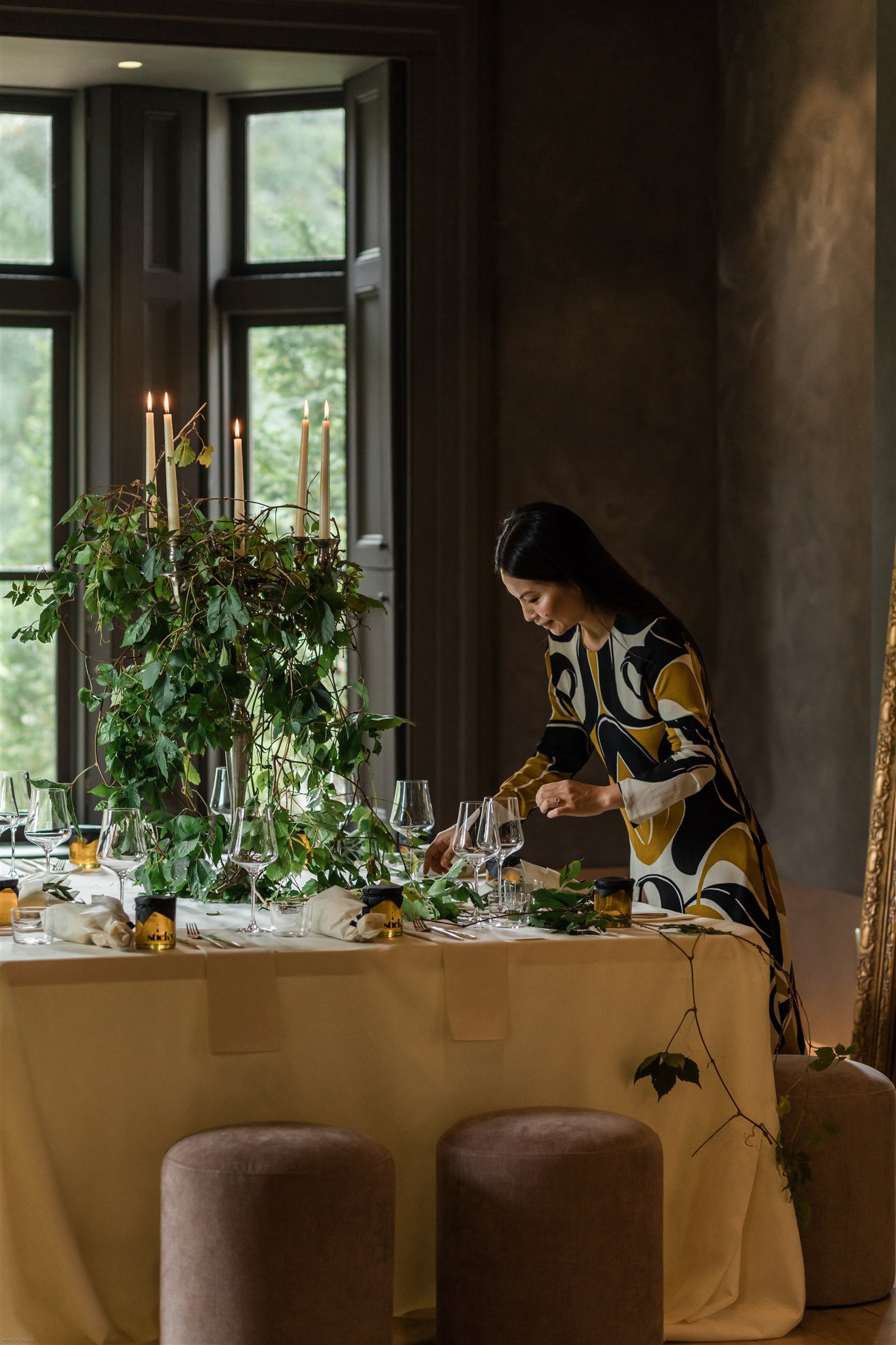 woman places final touches on an elaborately set dinner table, large lit candelabra covered in vines sits in the middle of the table