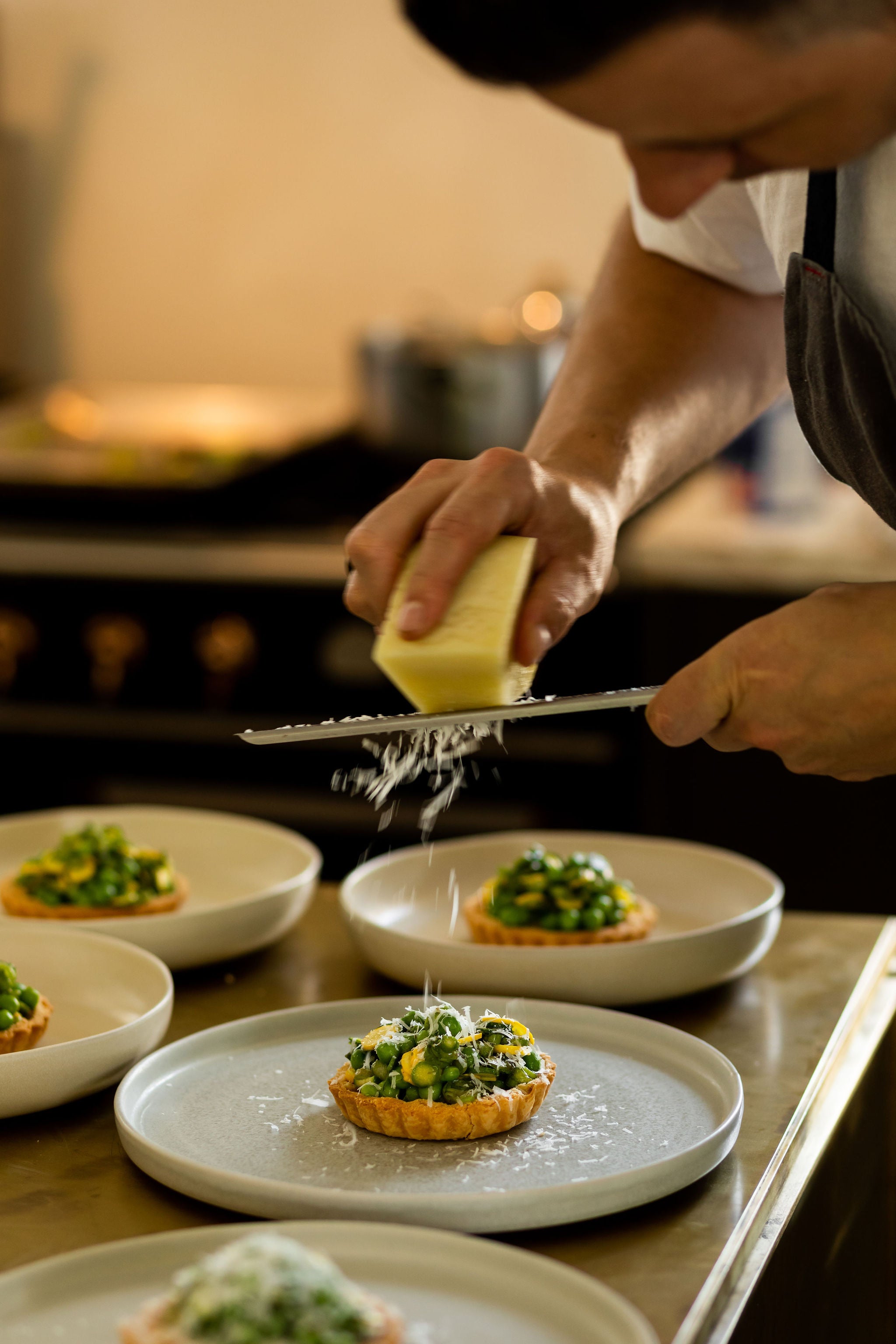 chef grates cheese on top of vegetable tart