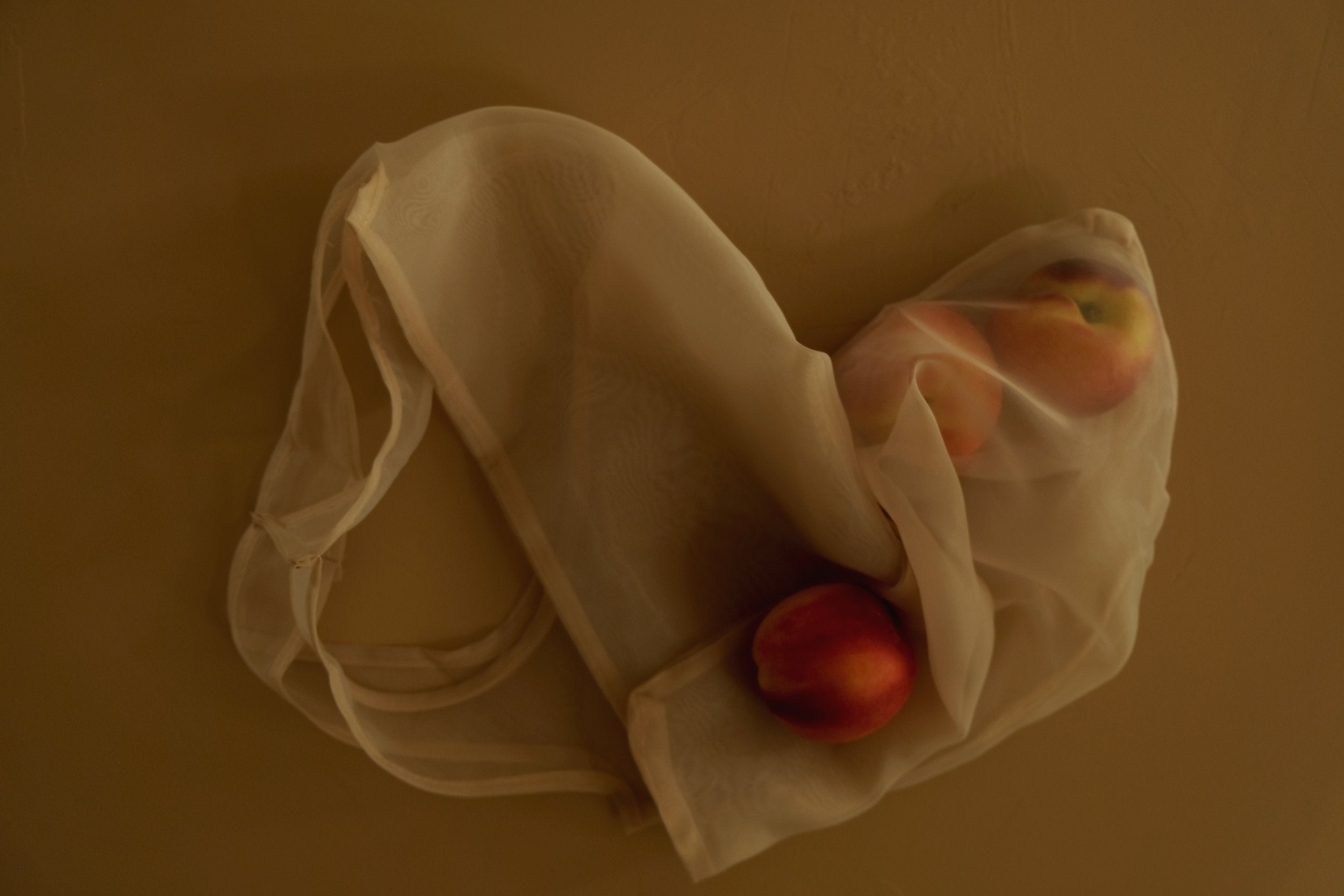 peaches sit on a table inside an organza tote