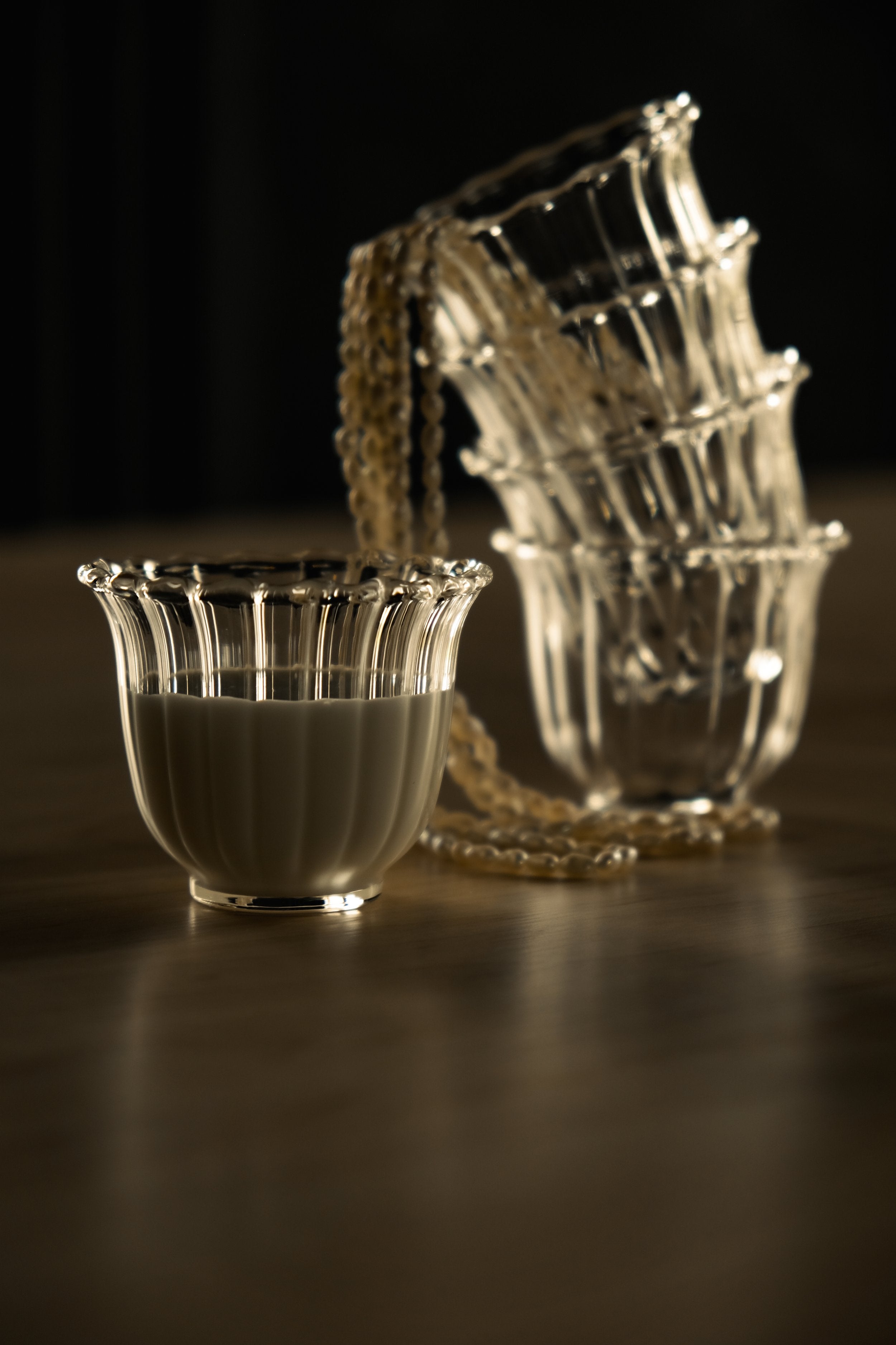 glass of milk sits in front of a stack of 4 of the same glass, a string of pearls cascades out of the top glass
