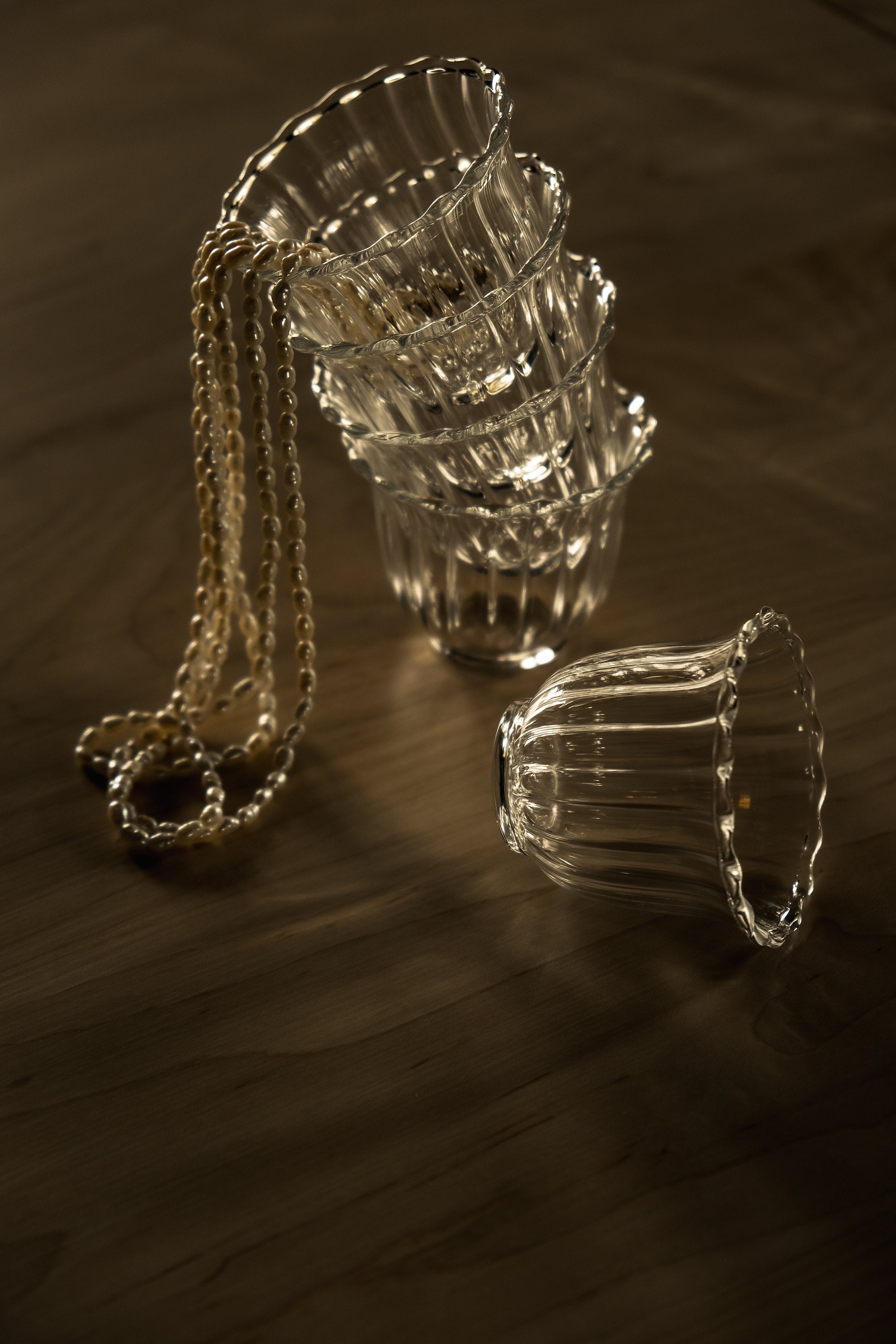 empty glass sits in front of a stack of 4 of the same glass, a string of pearls cascades out of the top glass